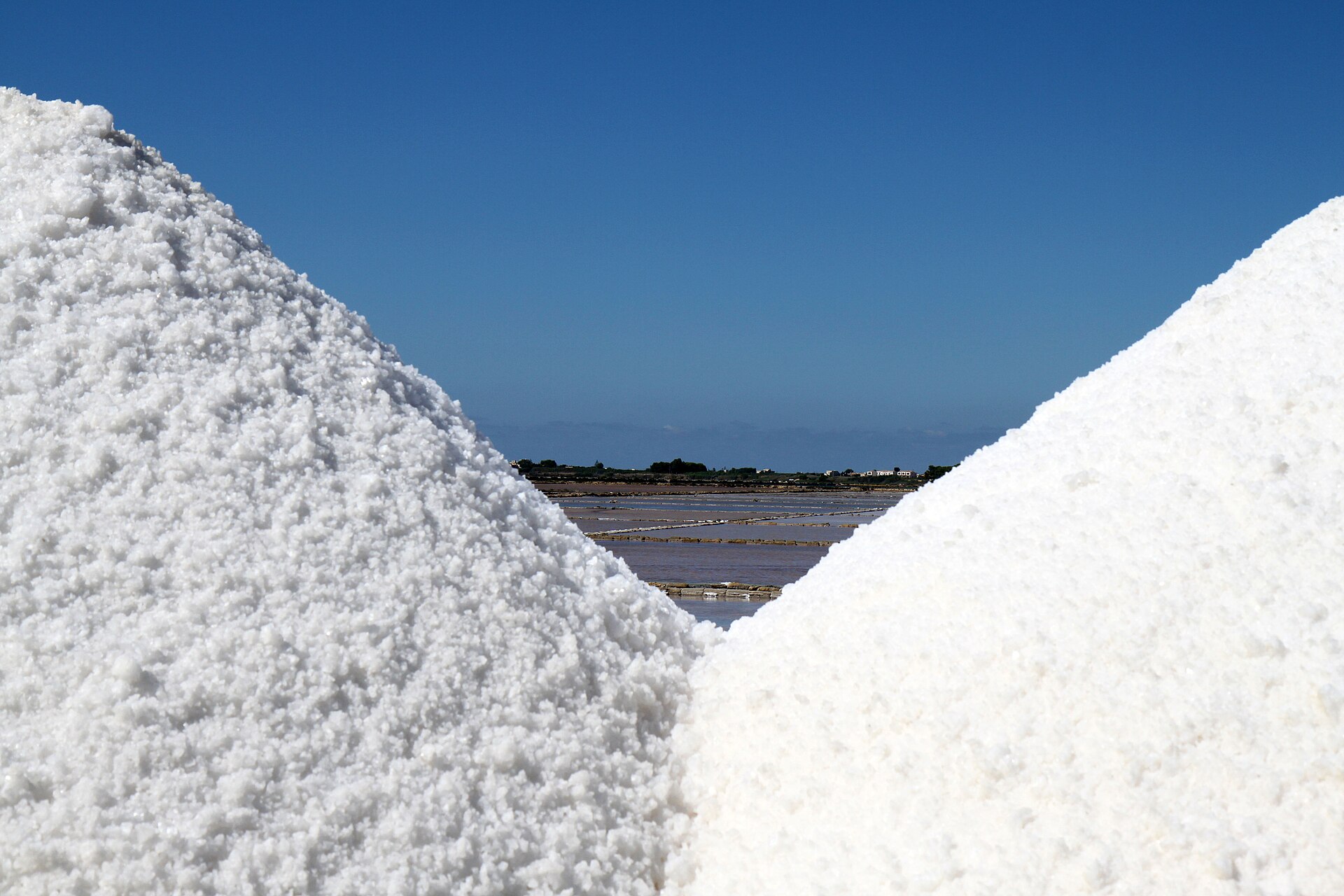 Cumuli di sale bianco nelle saline con le vasche sullo sfondo