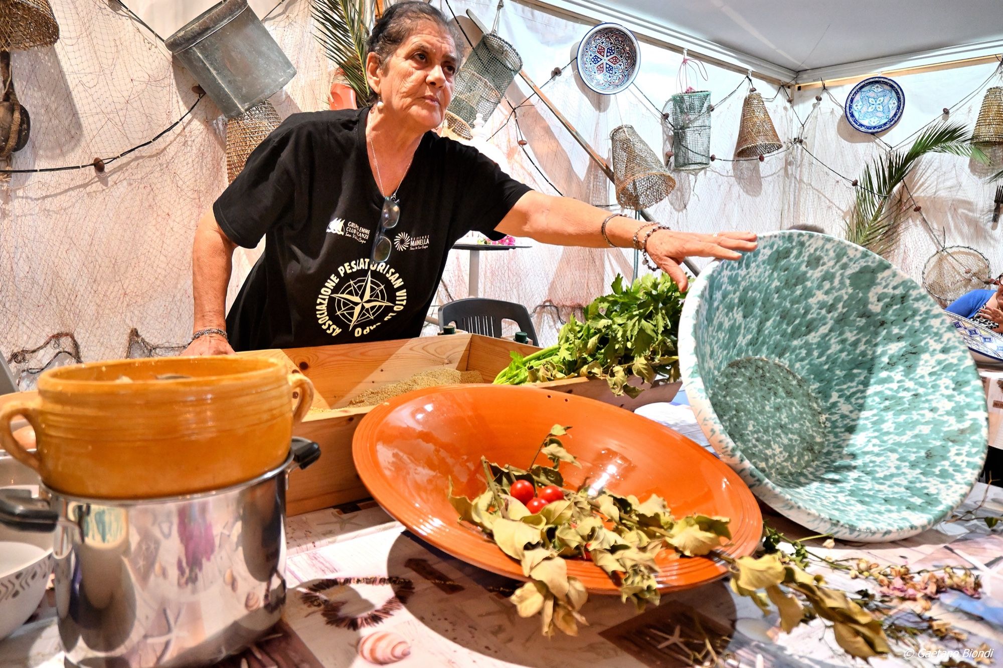La moglie di un pescatore spiega la preparazione del cous cous mostrando una ciaramira utiizzata per le grosse tavolate